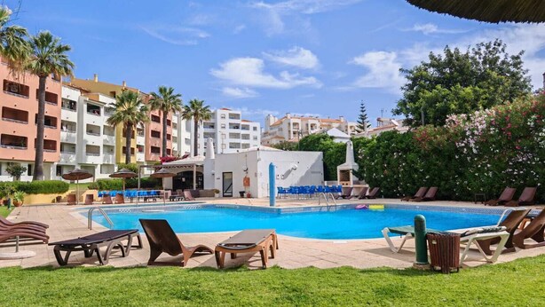 A pool area with lounge chairs, a covered seating area, and a building with balconies. - Casa DiLauNa - Cozy apartment in the heart of Albufeira - Portugal (Albufeira)
