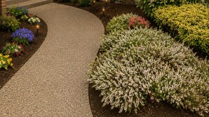 Een huis met een overdekte veranda, een grote boom en een aangelegde tuin met verschillende planten en bloemen.