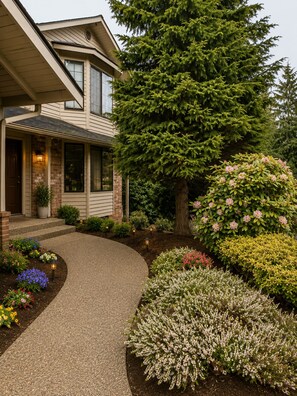A house with a covered porch, a large tree, and a landscaped garden with various plants and flowers. - World Cup Cozy Family Retreat, 4BR, 3 Living Rooms, Deck & Fenced Yard (Everett)
