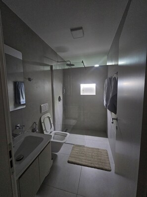 Ein modernes Badezimmer mit Toilette, Waschbecken, Dusche und einem kleinen Fenster.