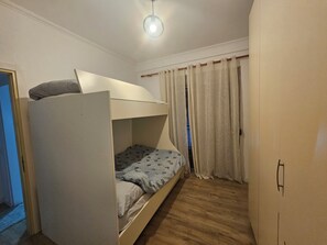 Ein Stockbett mit Kopfteil, Holzboden, Tür und Vorhang.