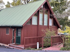 Uma cabana de madeira com telhado verde, varanda frontal e um pequeno deck.