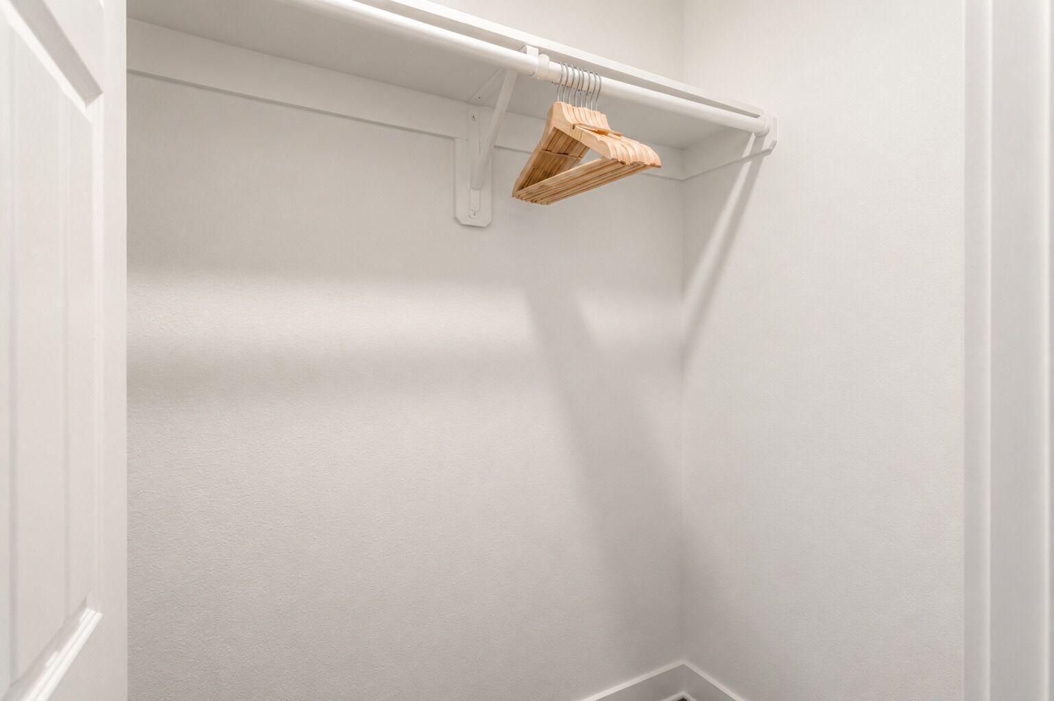 Un armadio bianco con una rastrelliera per appendini in legno.