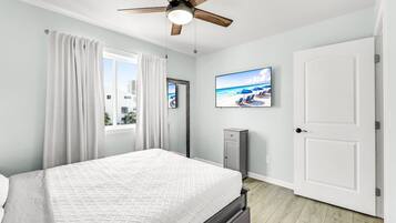 A bedroom with a bed, a ceiling fan, a TV on the wall, and a door.