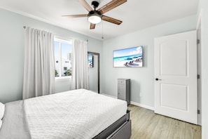 A bedroom with a bed, a ceiling fan, a TV on the wall, and a door. - 100 Yards to Beach! Fire Pit, 3 Decks, Dogs OK! (Navarre)