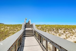 A wooden boardwalk leading to a building with a flag, surrounded by sand dunes. - 100 Yards to Beach! Fire Pit, 3 Decks, Dogs OK! (Navarre)