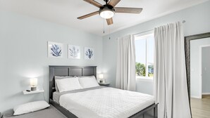 Ein Schlafzimmer mit einem Bett, Nachttischen, einem Deckenventilator und Kunstwerken an der Wand.