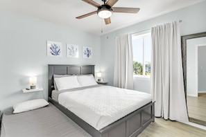 Un dormitorio con una cama, mesitas de noche, un ventilador de techo y obras de arte en la pared.