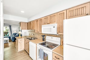 A modern kitchen with wooden cabinets, a white microwave, a stove, and a dishwasher. - 100 Yards to Beach! Fire Pit, 3 Decks, Dogs OK! (Navarre)