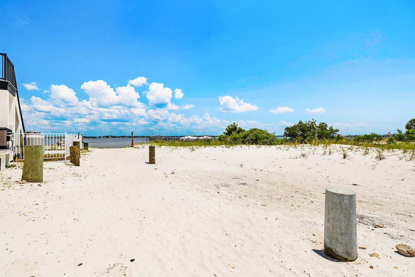 A sandy beach with a clear sky, a body of water in the distance, and a building with a white facade on the left.