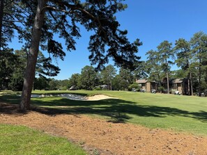Ein Golfplatz mit Sandbunkern, einem Clubhaus und umliegenden Bäumen.