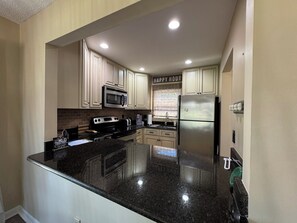 A kitchen with white cabinets, a stainless steel refrigerator, a microwave, a stove, and a granite countertop. - 2Bed2Bath Condo w/ Fairway Views on No. 5: Walk to Club, Cradle & Harness Track (Pinehurst)