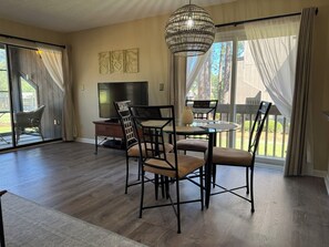 A dining area with a glass table, chairs, a chandelier, and a television. - 2Bed2Bath Condo w/ Fairway Views on No. 5: Walk to Club, Cradle & Harness Track (Pinehurst)