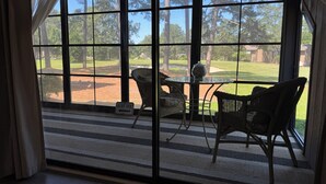 Ein Zimmer mit großen Fenstern, Korbmöbeln und Blick auf einen Golfplatz.
