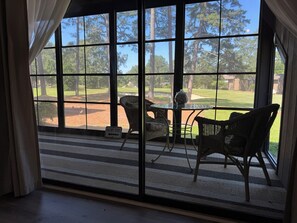 Ein Zimmer mit großen Fenstern, Korbmöbeln und Blick auf einen Golfplatz.