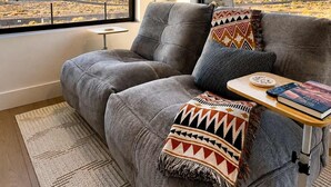 A modern living room with a grey sofa, patterned cushions, a small table, and a view of a desert landscape through large windows. - The Dark Sky Haven, Luxe Casita, Views, Sleeps 2 (Page)