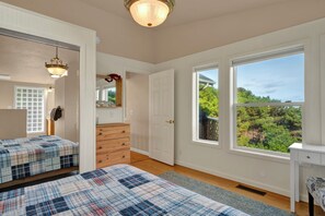 Ein Schlafzimmer mit zwei Betten, einem Schminktisch, einem Spiegel und großen Fenstern mit Blick auf Grünflächen.