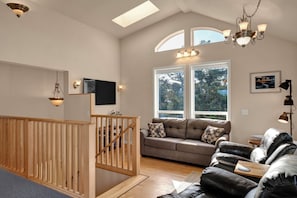 Ein geräumiger Wohnbereich mit einer Holztreppe, einem Sofa, einem Ledersessel und einem an der Wand montierten Fernseher.