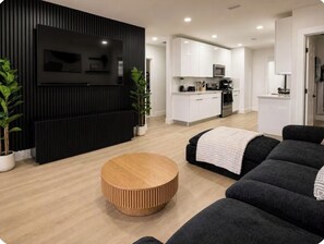 Een moderne woonkamer met een ronde houten salontafel, zwarte banken en een accentmuur in het zwart.