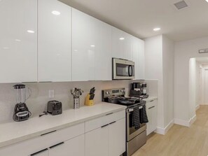 A modern kitchen with white cabinets, a microwave, a stove, a blender, and a toaster. - Wilton Manors • Las Olas • Beach • Downtown FTL (Fort Lauderdale)