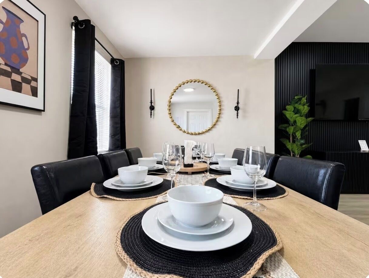 A dining area with a wooden table set for six, black chairs, a mirror, and a black wall with a television.