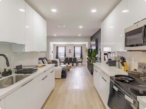 A modern kitchen with white cabinets, a dining area with a table and chairs, and a large window providing natural light. - Wilton Manors • Las Olas • Beach • Downtown FTL (Fort Lauderdale)