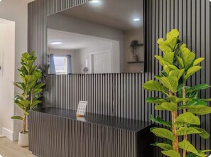A reception desk with a large mirror, two potted plants, and a sign. - Wilton Manors • Las Olas • Beach • Downtown FTL (Fort Lauderdale)