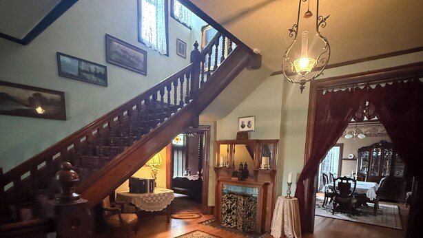 A spacious living area with a wooden staircase, a large patterned rug, and a chandelier.