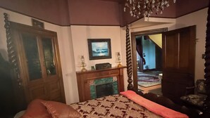 A bedroom with a large bed, a chandelier, a fireplace, and a view of a staircase.