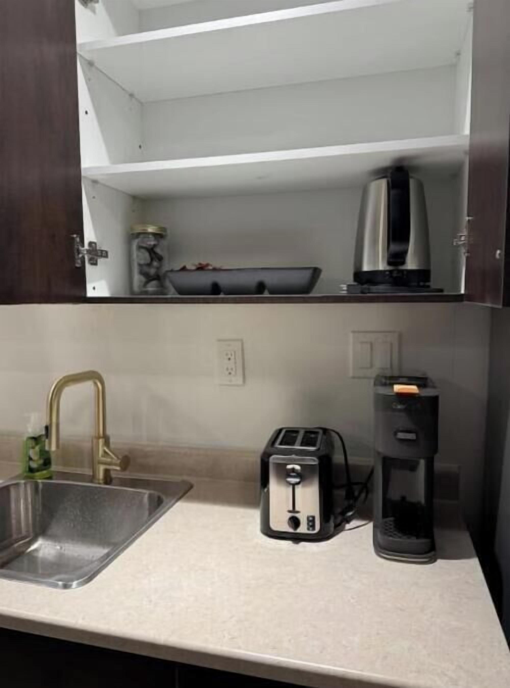 Uma cozinha compacta com pia, torradeira, cafeteira e um pote sobre a bancada.