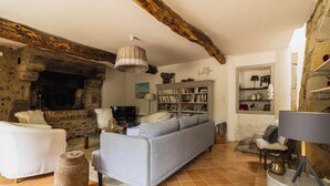 Ein rustikales Wohnzimmer mit Kamin aus Stein, einer Couch, einem Bücherregal und einem Fernseher.