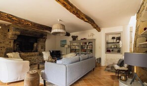 A rustic living room with a stone fireplace, a sofa, a bookshelf, and a television. - Authentic Breton farmhouse | 8 guests | Ref 307 (PLEBOULLE)