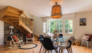 A dining area with a glass table, black chairs, a wooden staircase, and a hanging light fixture. - Authentic Breton farmhouse | 8 guests | Ref 307 (PLEBOULLE)