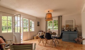 A dining area with a table, chairs, a hanging light fixture, and a view through large windows. - Authentic Breton farmhouse | 8 guests | Ref 307 (PLEBOULLE)