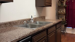 A kitchen with granite countertops, a dishwasher, and wooden cabinets. - Victorian Fairy Cottage (Houston)