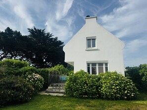 Ein weißes Haus mit Satteldach, einem kleinen Fenster und einem Schornstein.
