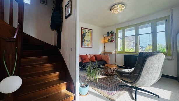 Eine Treppe führt zu einem Wohnbereich mit einer Couch, einem Sessel und einer Topfpflanze.