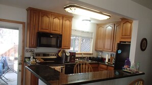 Una cocina con armarios de madera, microondas negro, estufa y refrigerador. Cuenta con una barra con dos sillas.