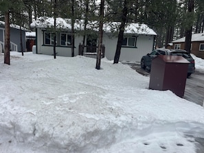 Ein Wohngebiet mit schneebedecktem Boden, einem parkenden Auto und einem Haus mit sichtbarer Garagentür.