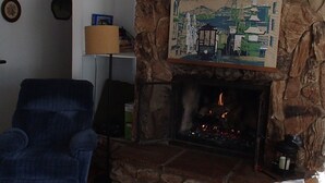 Una sala de estar con chimenea de piedra, un sillón azul y un cuadro sobre la chimenea.
