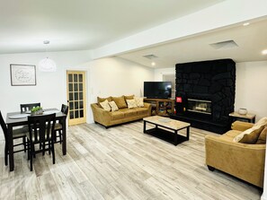 A living room with a fireplace, a TV, a dining area with chairs and a table, and a sofa. - Adorable 4-bedroom home in a peaceful Pocono Lake with a hot tub! (Pocono Lake)