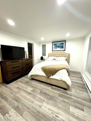 Ein Schlafzimmer mit Bett, Schminktisch, Fernseher und einem gerahmten Bild an der Wand.