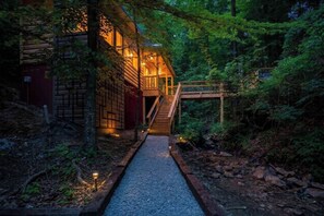 Eine Blockhütte mit einer Holztreppe, die zu einer Terrasse führt, umgeben von dichtem Wald.