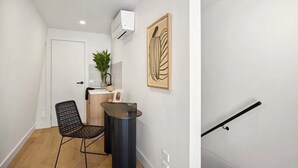 Een modern interieur met een houten vloer, een zwarte mesh-stoel, een klein tafeltje en een wandairconditioner.