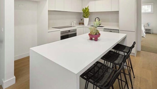 Een moderne keuken met witte kasten, een centraal eiland met barkrukken en een potplant.