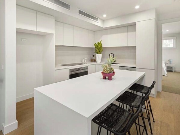 A modern kitchen with white cabinetry, a central island with bar stools, and a potted plant. - Urban Delight (Burnley)