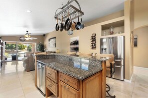 A kitchen with a granite countertop, wooden cabinets, a stainless steel refrigerator, and a ceiling fan. - Lakefront Oasis | Infinity Edge Pool & Golf Views (Glendale)