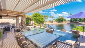 An outdoor pool area with lounge chairs, a table, and a pergola structure. - Lakefront Oasis | Infinity Edge Pool & Golf Views (Glendale)