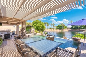An outdoor pool area with lounge chairs, a table, and a pergola structure. - Lakefront Oasis | Infinity Edge Pool & Golf Views (Glendale)