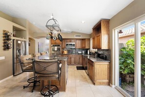 A modern kitchen with wooden cabinets, a central island, and a dining area with a chair. - Lakefront Oasis | Infinity Edge Pool & Golf Views (Glendale)